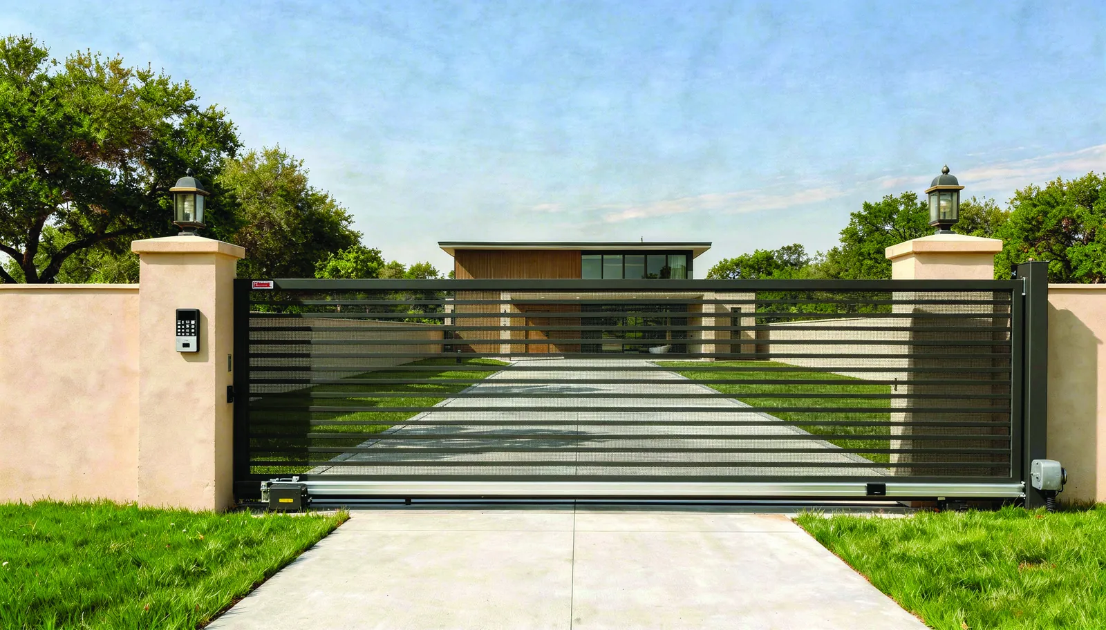 A sliding metal gate between stone pillars at the entrance of a home with a lawn