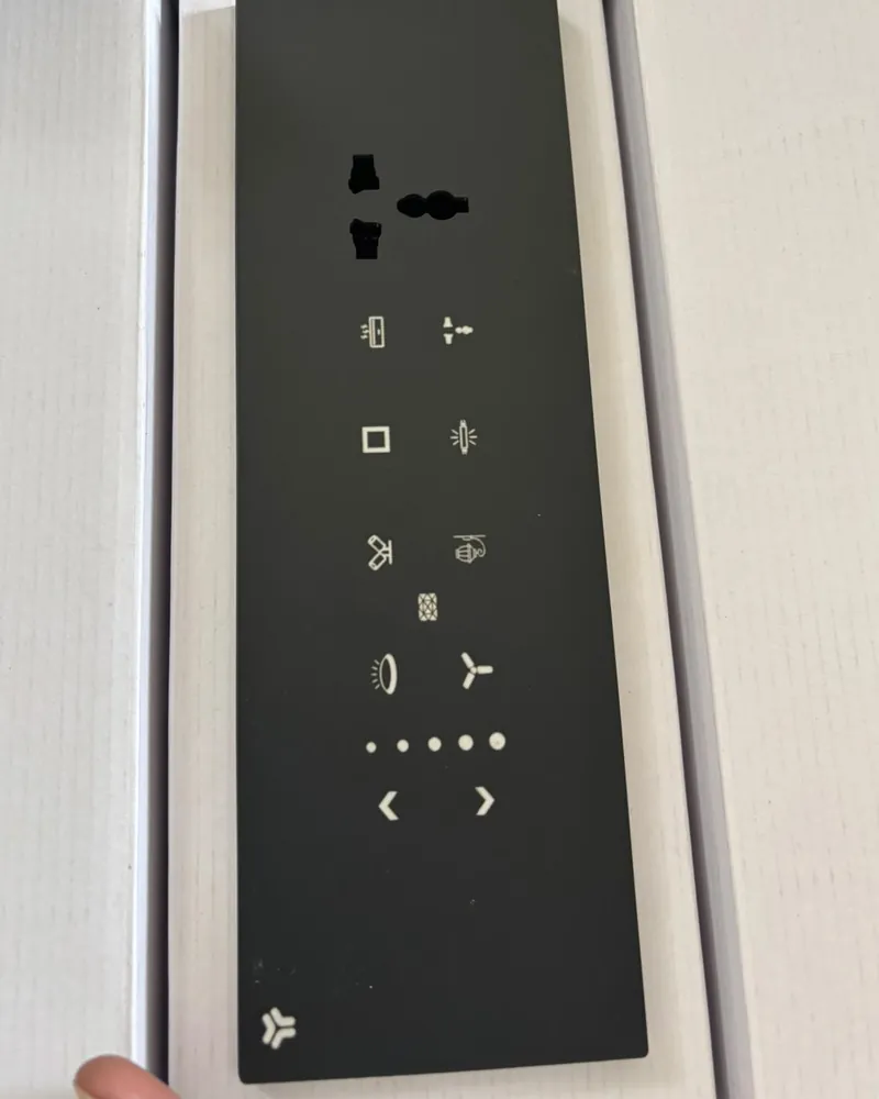 A tall black glass touch panel with a socket and backlit icons, in its box