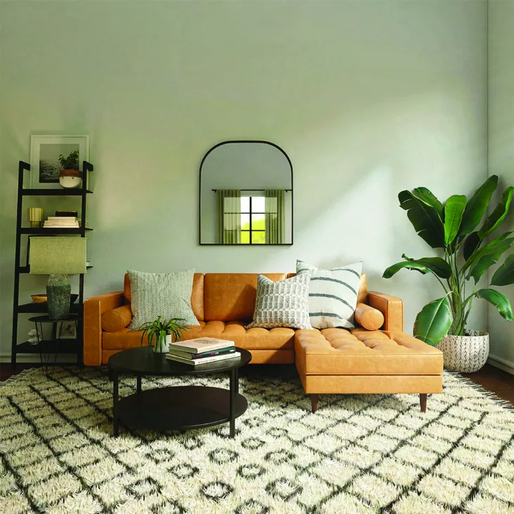 A living room with a tan sofa, patterned rug and a black scene keypad on the wall