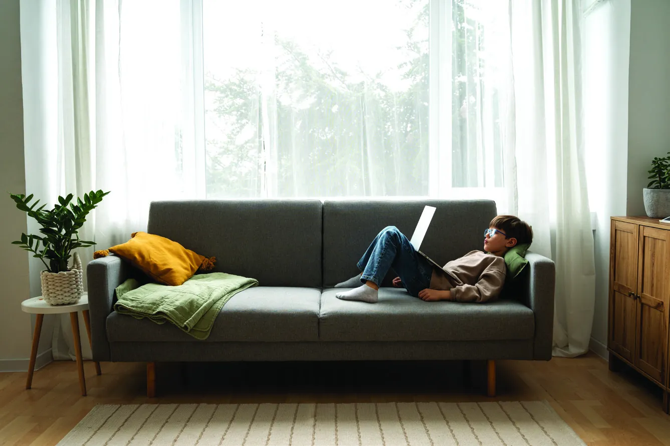 A child lying on a sofa with a laptop in a softly lit living room